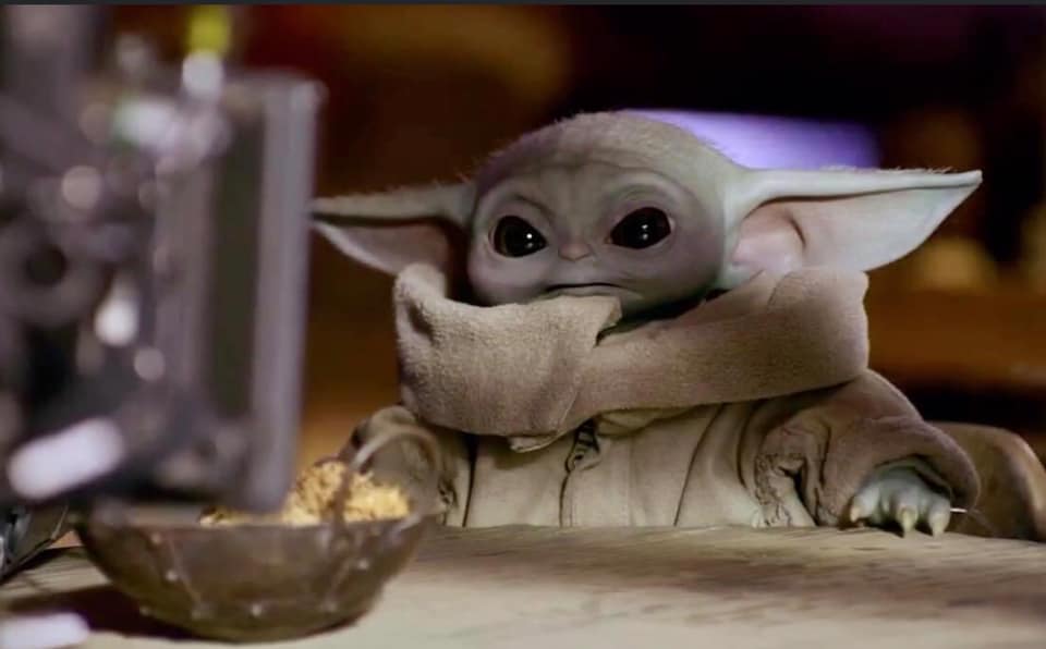 The meme is a screenshot of the character Baby Yoda from the Star Wars series "The Mandalorian". The image shows Baby Yoda sitting at a table, looking up at a screen with a surprised expression, as if he's watching something fascinating. The text "I love sitcoms" appears in a speech bubble above Baby Yoda's head.